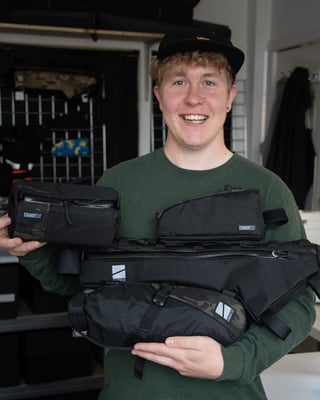 Ross O'Reilly of Straight Cut Design holds a handlebar bag, top tube bag, frame bag and seat pack in his studio.