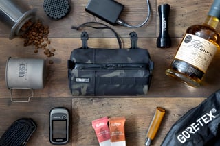 Straight Cut Design camouflage handlebar bag laid out flat with coffee, whisky, a GPS and other bikepacking kit.