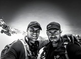 Adventure Patch Company founders Chris and Dom in a black and white selfie below a snowy ridge.