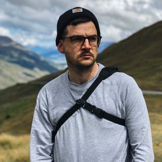 Skin Grows Back 3Point Cycling Camera Strap worn across the chest of a person in a beanie, with hills behind.