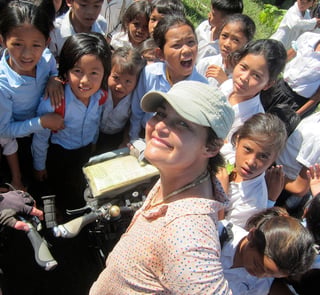 Smiling cyclist takes a selfie with a crowd of uniformed schoolchildren gathered around a touring bike.