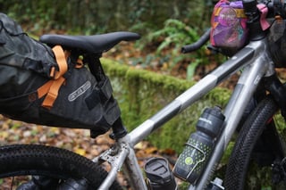 Ortlieb seat pack and a bottle on the Riverside 920 prototype frame, with a handlebar pouch and mossy wall behind.