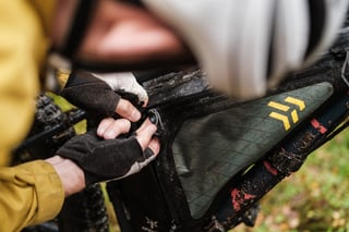 Rider zips open a muddy Apidura Backcountry frame pack on a mountain bike.