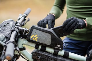 Rider fits a phone mount on top of an Apidura Backcountry top tube pack on a muddy mountain bike.