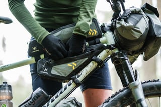 Rider fits an Apidura Backcountry top tube pack above the frame pack, with a handlebar pack on the bars.
