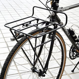 Pass and Stow black front rack on a Surly Cross-Check with tan-wall knobbly tyres, parked on a tiled pavement.