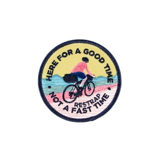 Restrap embroidered patch of a bikepacker riding past hills, reading 'Here for a good time, not a fast time'.