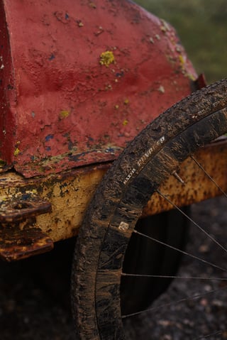Mud-covered Maxxis Ravager tyre beside a rusty red farm machine, with the sidewall lettering still visible.