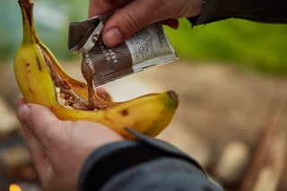 Outdoor Provisions nut butter squeezed from its sachet into a split banana, the start of a campfire banana boat.