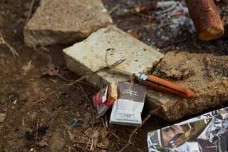 Opened nut butter sachet, bar wrapper and a wooden-handled knife on a fire stone beside the campfire.