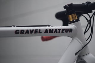 Close-up of the Gravel Amateur lettering on the white top tube, with gold spacers and a black stem.