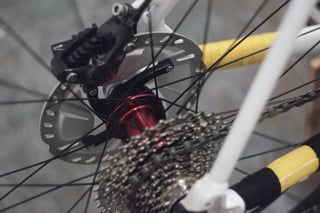 Red rear hub of the custom Ryanbuildswheels wheelset, with cassette, disc rotor and yellow chain stay wrap.