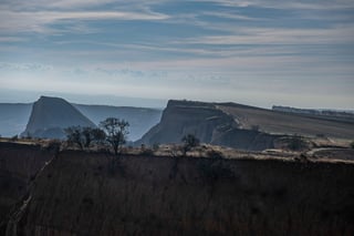Eroded clay cliffs and flat-topped hills in an arid landscape under a hazy sky.