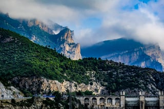Rocky cliffs wreathed in cloud above a wooded slope and a concrete dam on the European Divide Trail route.