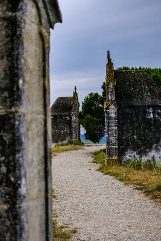 Gravel path between weathered stone mausoleums with Gothic pinnacles under a grey sky.