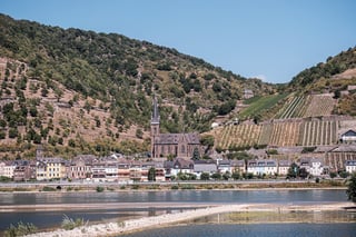 Riverside town with a Gothic church spire and terraced vineyards on a steep hillside, on the European Divide Trail.