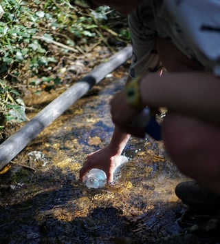 Hand holds a Katadyn BeFree flask under the surface of a clear stream to fill it with water.