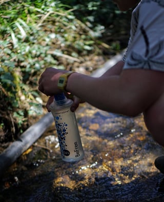 Rider screws the filter lid onto a filled Katadyn BeFree 0.6L flask beside a stream.
