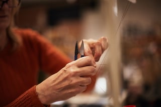 Hands snip a loose thread with small sprung clippers at a Restrap sewing station.