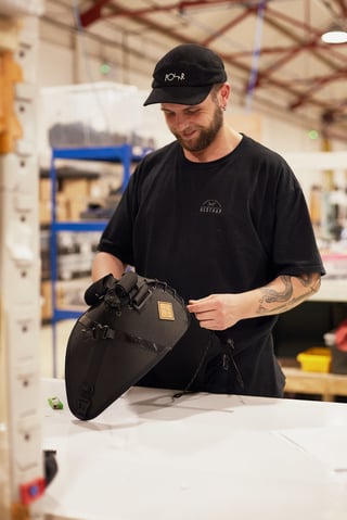 Finisher in a Restrap T-shirt and cap laces up the holster of a black saddle pack at the packing bench.