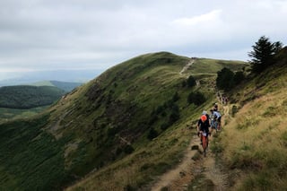 Grinduro 2021 riders climb a narrow singletrack path along a steep grassy ridge in mid Wales.