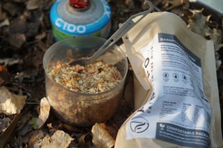 Firepot Barbecued Pulled Pork tipped from its compostable packet into a clear cup, with a spork and gas canister behind.