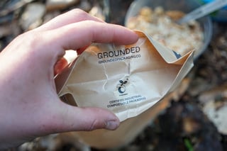 Hand holding open a Firepot compostable packet printed with Grounded and certified industrial compostable packaging.