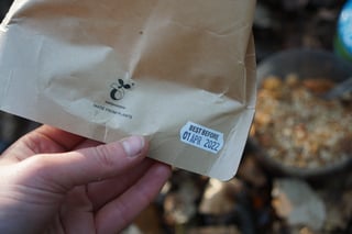 Hand holding the back of a Firepot compostable packet, showing its best before date label.