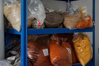 Bags of ground spices and dried ingredients on blue shelving in the Firepot Food kitchen store in Dorset.