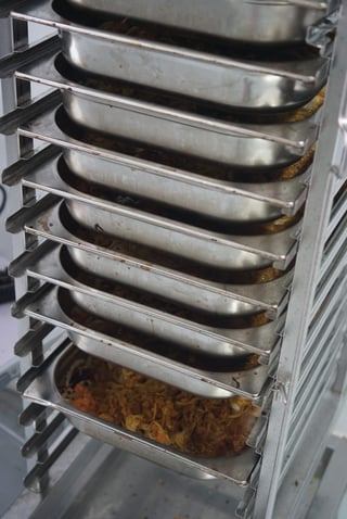 Stainless steel trays of freshly cooked meal mix stacked on a trolley at Firepot Food before air drying.