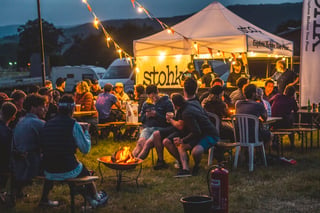 Riders gather round a fire pit and the Stohk drinks tent at dusk at the Grinduro 2021 campsite in Wales.