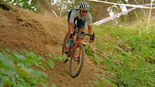 Claire Frecknall drops a steep dusty bank on an orange gravel bike between course tape at Grinduro 2021.