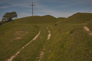 Grassy, rutted track climbing towards a wooden cross on a hilltop in Dorset, near the end of the Lyme Regis ride.