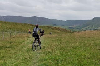 Rider on a hardtail mountain bike heads across a grassy field towards the Welsh hills at Grinduro 2021.