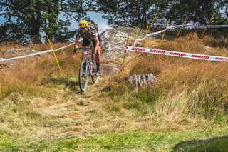 Rider in a yellow helmet rolls through long grass between SRAM course tape at Grinduro 2021 in Wales.