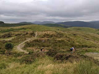 Riders follow a winding gravel path over open moorland under grey skies on the Grinduro 2021 route in Wales.