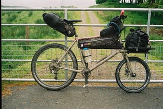 Side view of the Rothair mini cargo bike at a gate, with knobbly tyres, Farr Out frame bag, seatpack and front rack bag.