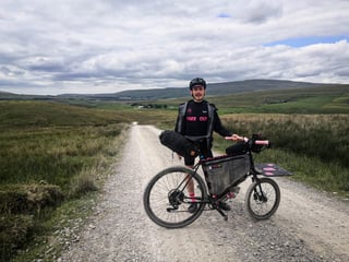 Farr Out Deliveries rider stands with the Rothair cargo bike on a gravel track above a wide moorland valley, Pennine Rally.