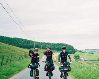 Three Farr Out Deliveries riders with bikepacking bags ride towards the camera on a quiet lane during the Pennine Rally.