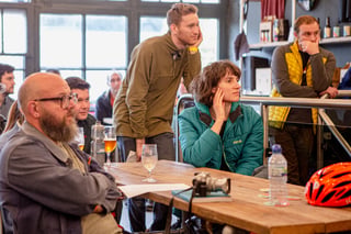 Audience at a Bespoked 2021 talk watches the speakers, with beers, a camera and a red helmet on the table.