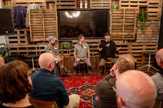 Three speakers sit on stools before a pallet-wood wall during the long-distance framebuilders panel at Bespoked 2021.