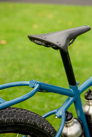 Brooks saddle above the looped blue rear rack and seat tube of the Clandestine Long Tail at Bespoked 2021.
