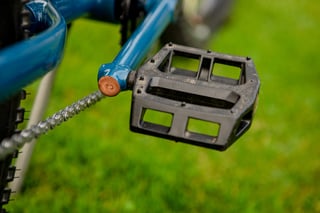 Black flat pedal on the custom crank of the Clandestine Long Tail, with a copper-capped pedal boss and chain behind.