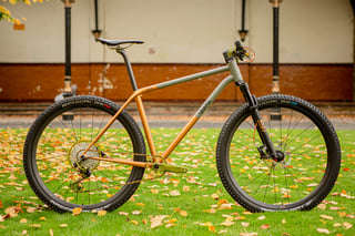 Quirk Cycles Superchub steel XC hardtail in copper and grey, with green anodised parts, on grass at Bespoked.
