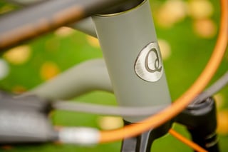 Brushed metal Quirk head badge on the grey head tube of the Superchub, with orange hose in the foreground.