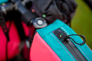 Close-up of a Wizard Works bag's zip pull and splatter-print webbing in teal and pink fabric.