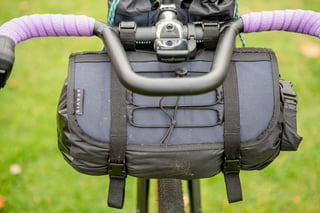 Aravis Bag Works handlebar holster with a bungee lattice mounted beneath drop bars wrapped in purple tape.