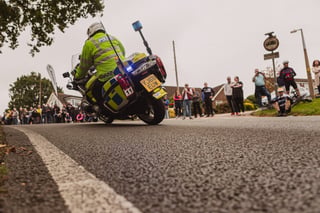 Police motorbike with blue lights on passes crowds on a suburban lane before the Women's Tour of Britain peloton.