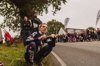 Kneeling spectator in cycling kit films the road as crowds line the Women's Tour of Britain route in South East Essex.