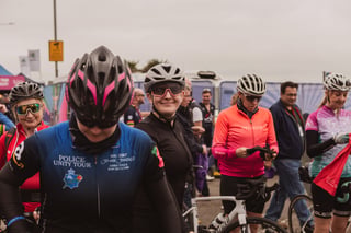 Riders in helmets gather in the Women's Tour of Britain finish area, one wearing a Police Unity Tour jersey.
